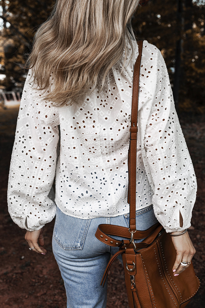 Person wearing a white blouse with eyelet design and blue jeans, holding a brown leather bag.