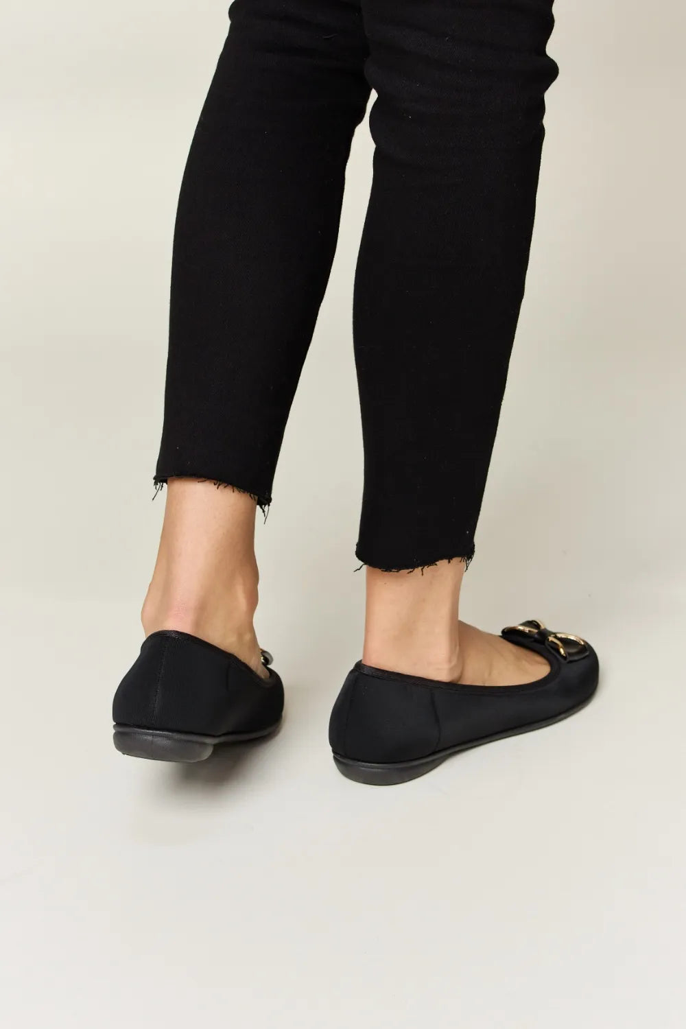 Person wearing black flat shoes and black pants on a light background
