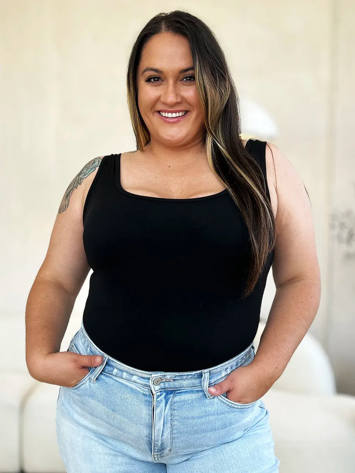 Woman wearing a black sleeveless top and light blue jeans indoors.