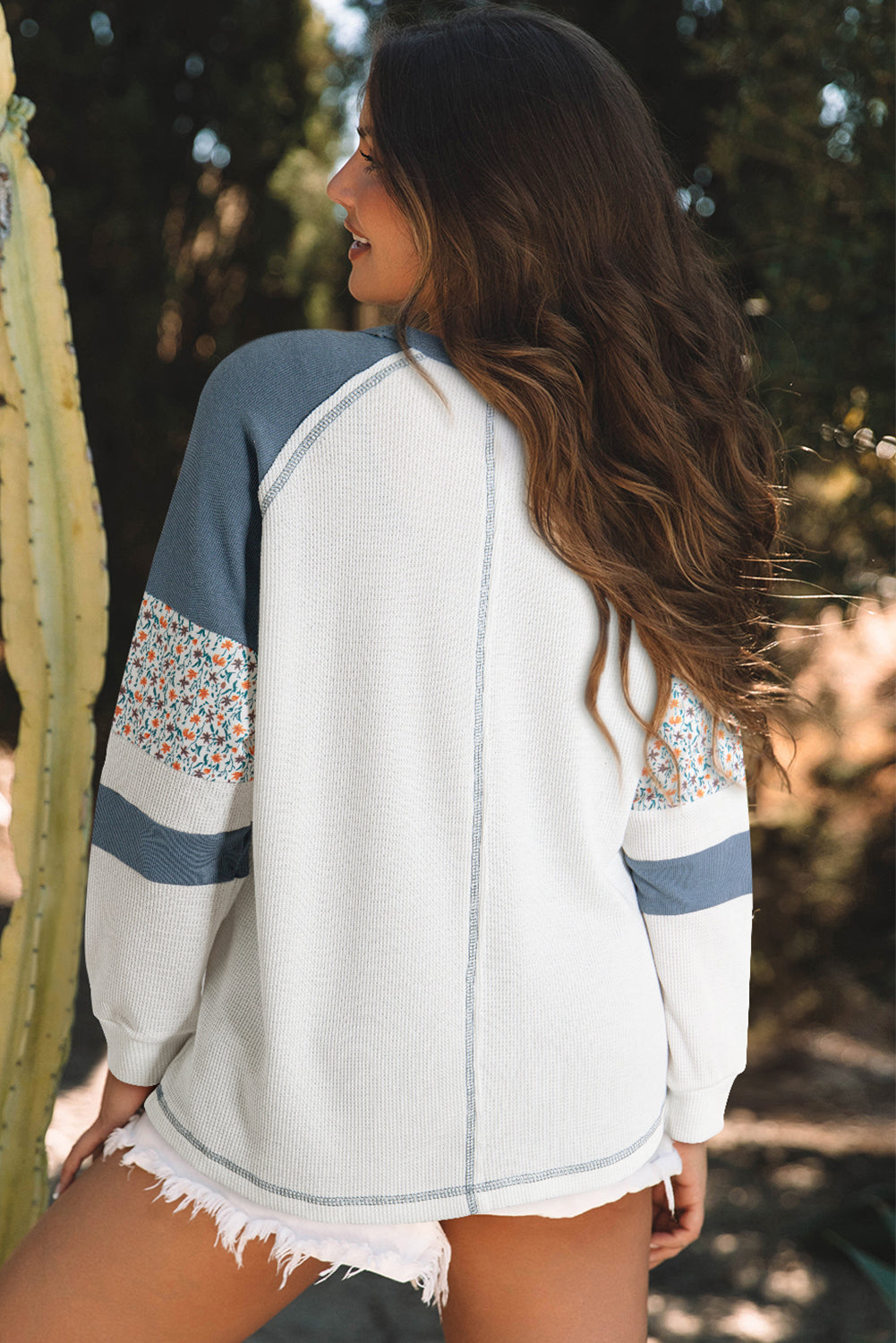 Woman wearing a white top with blue and floral sleeves, standing outdoors.