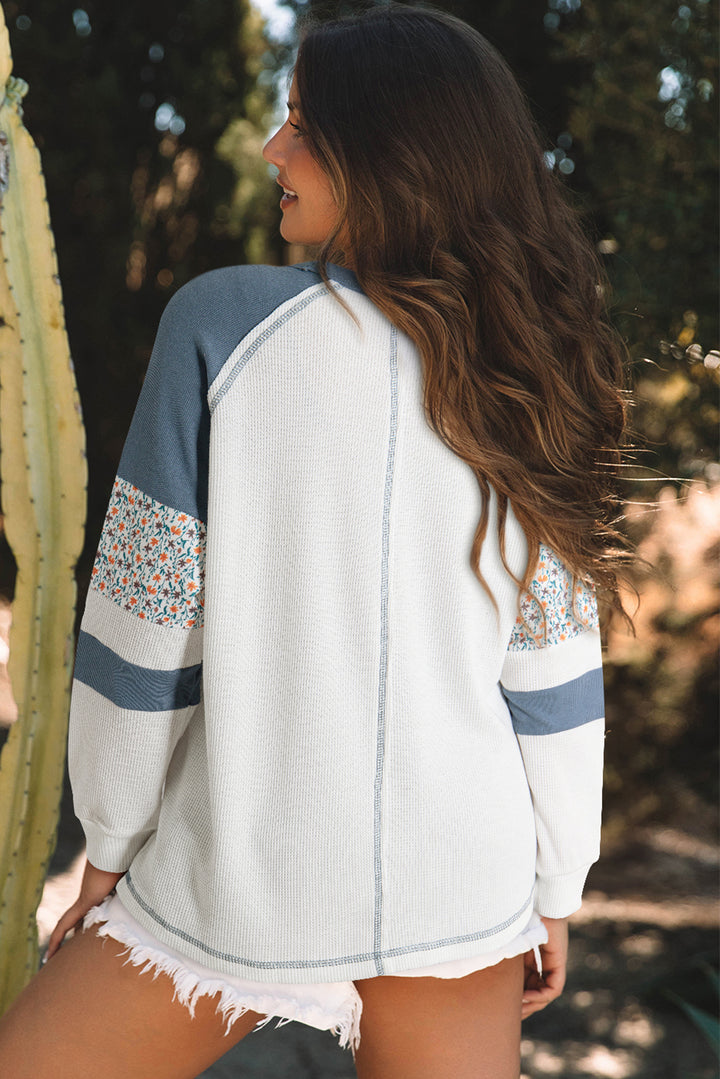 Woman wearing a white top with blue and floral sleeves, standing outdoors.