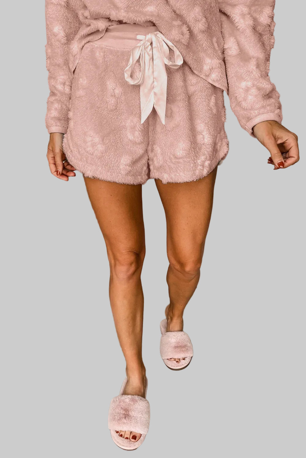 Person wearing a pink fluffy outfit with shorts and a top, standing next to a white background.