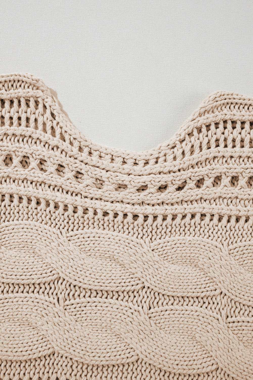 Close-up of a beige knitted garment with intricate patterns on a light gray background