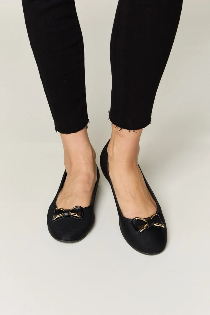 Black flats with gold accents worn with black pants on a white background