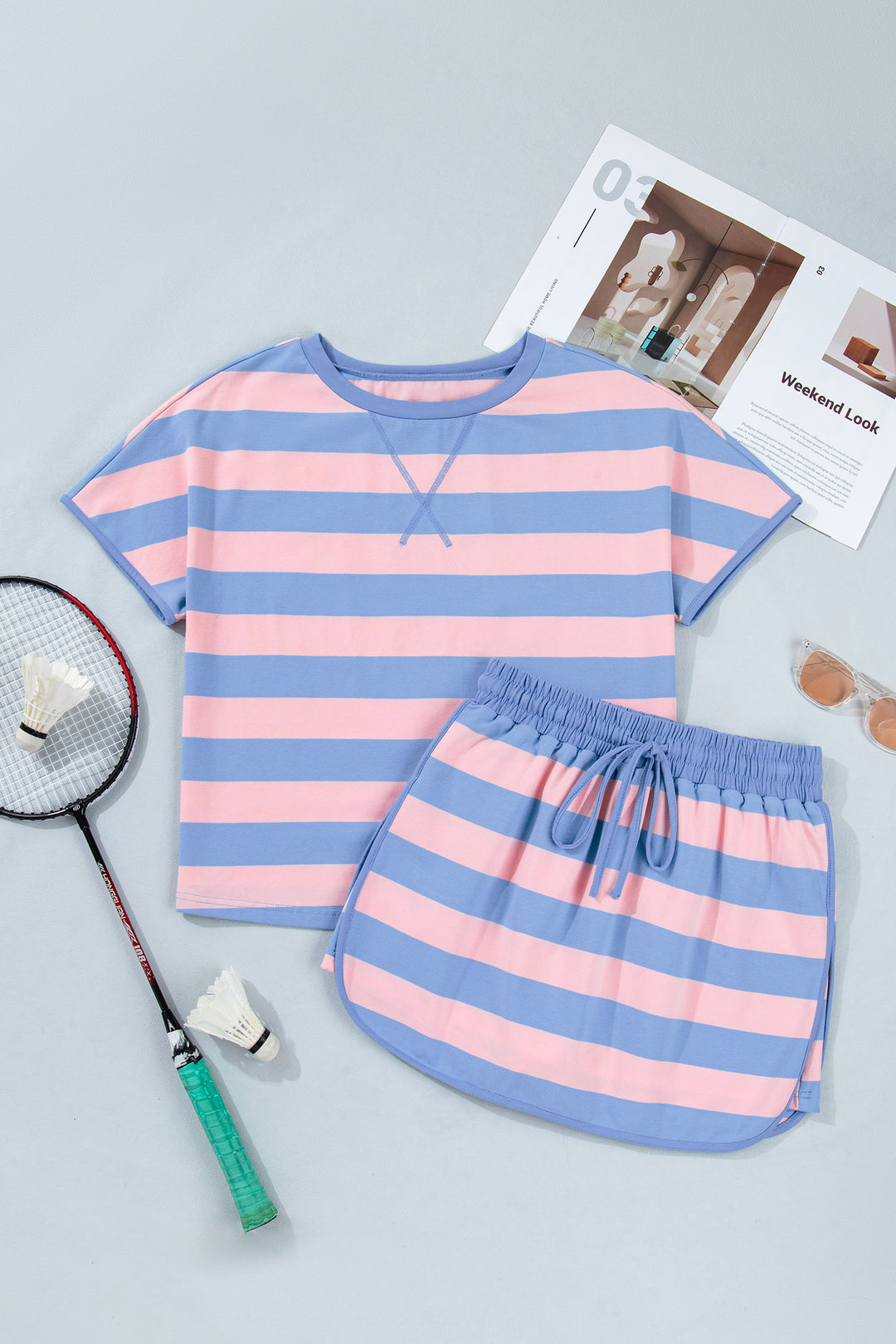 Pink and blue striped shirt and shorts set on a gray surface with a badminton racket and shuttlecock.