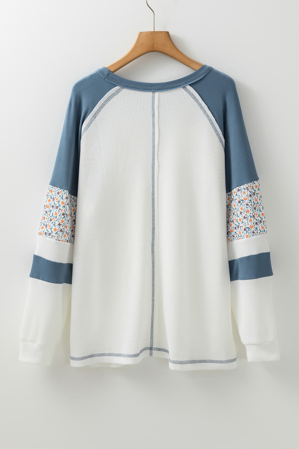 White shirt with blue sleeves and floral cuffs on a wooden hanger against a white background
