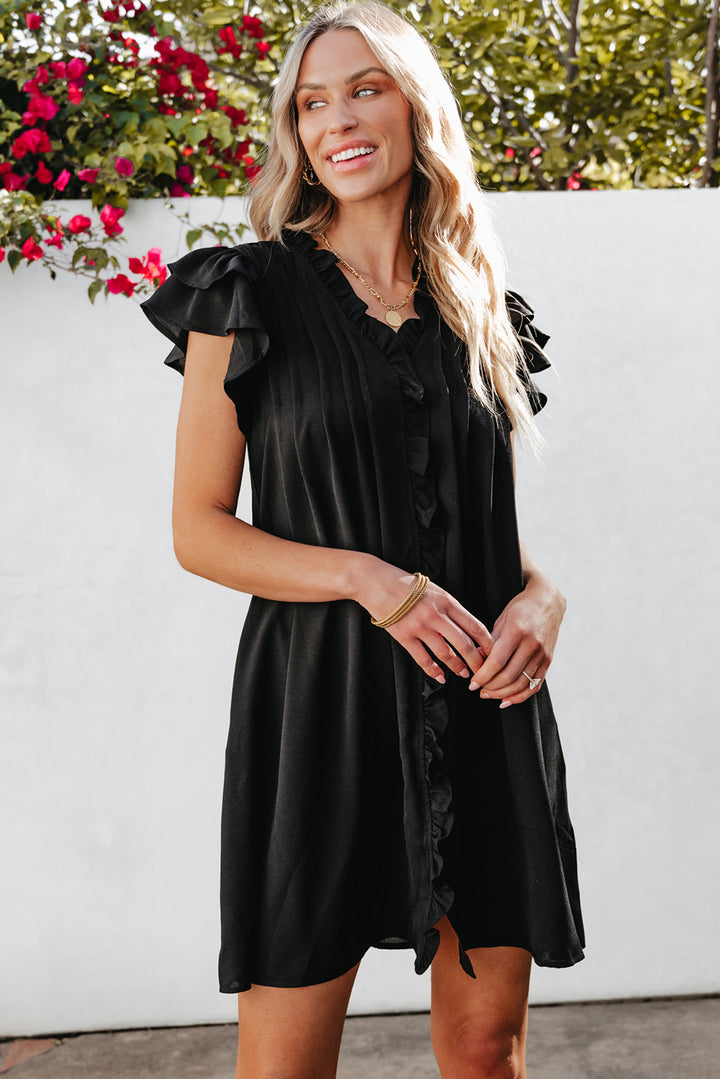 Woman wearing a black dress with ruffled sleeves in an outdoor setting.