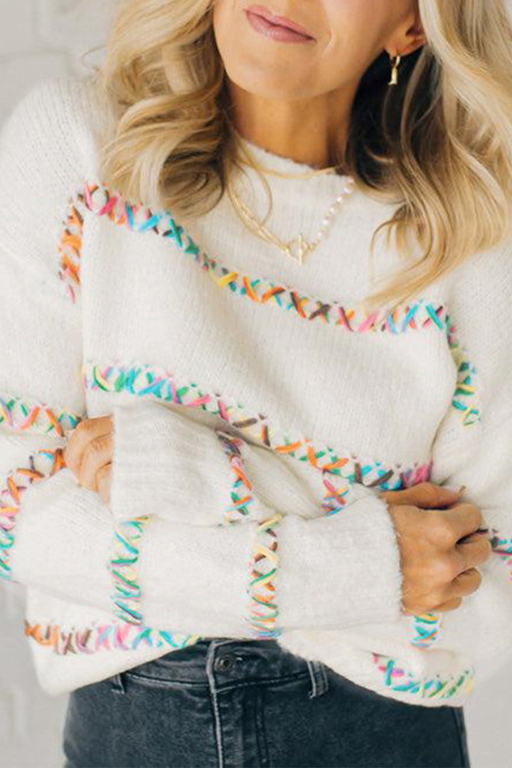 Woman wearing a white sweater with colorful trim, holding the sleeves.