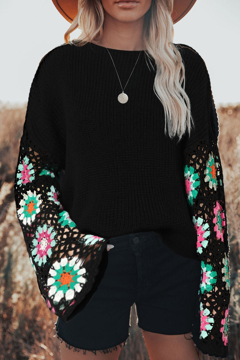 Person wearing a black sweater with colorful floral patterns on the sleeves against a neutral background.