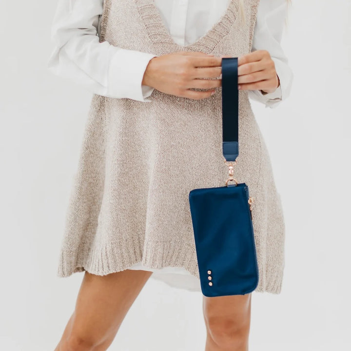 woman wearing a cream-colored dress holding a navy strapped wristlet wallet