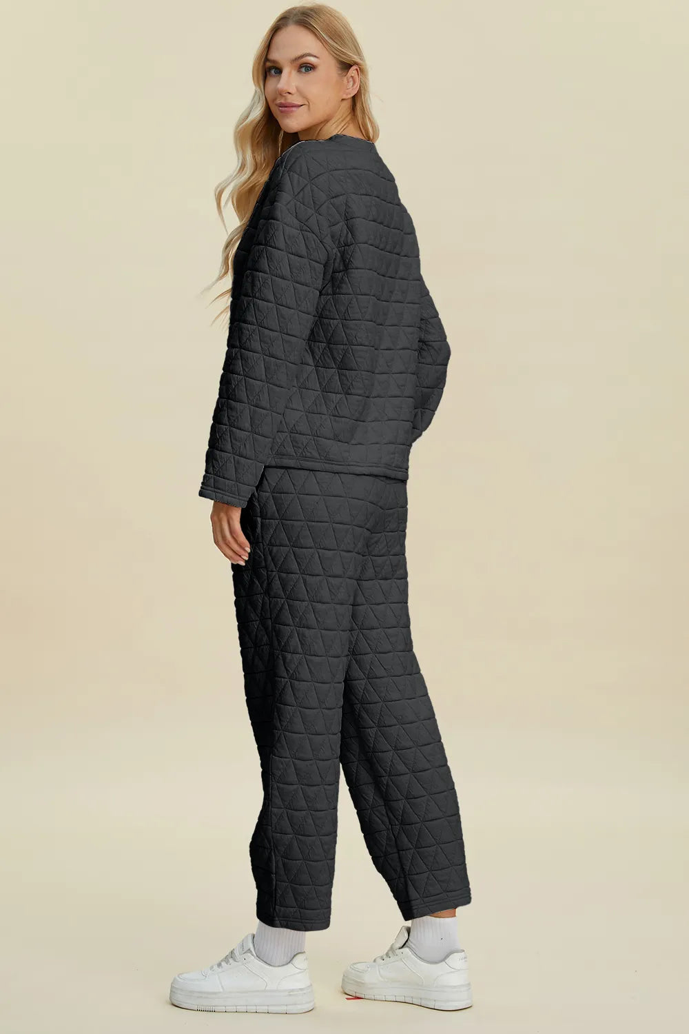 Woman wearing a dark gray quilted jacket and pants on a beige background