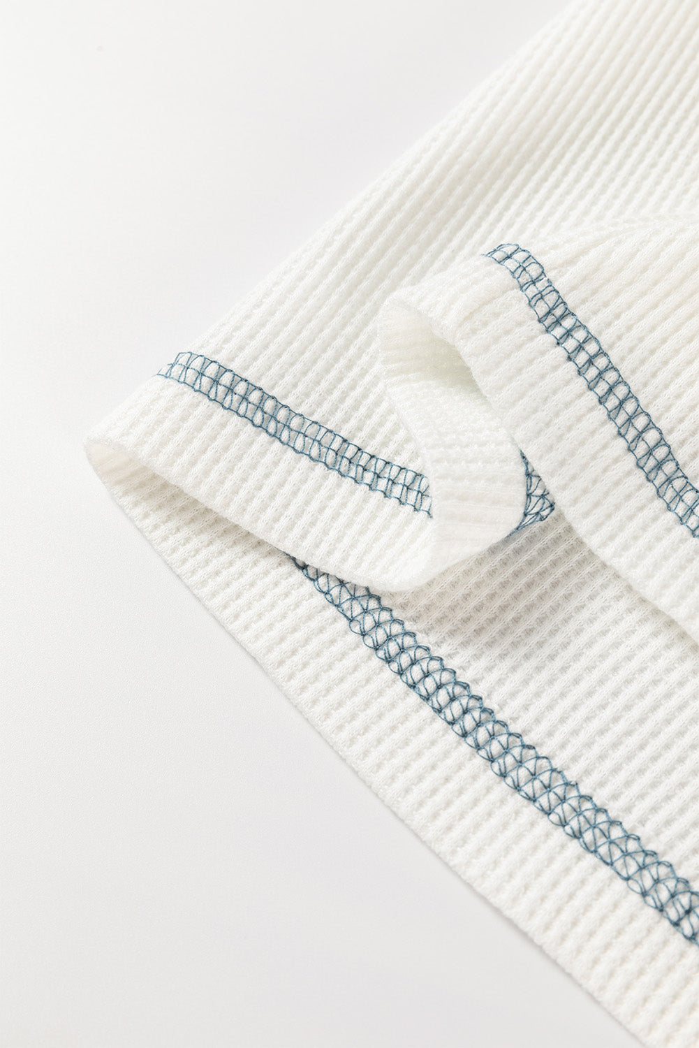 Close-up of a textured white top with blue stitching on a light gray background