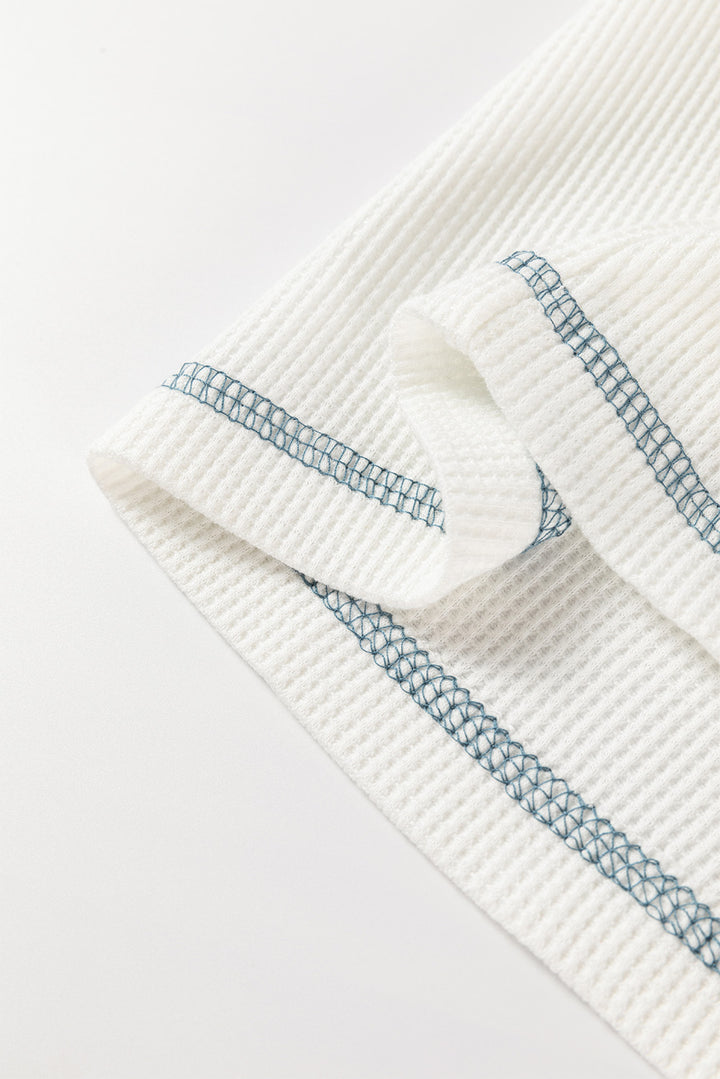 Close-up of a textured white top with blue stitching on a light gray background