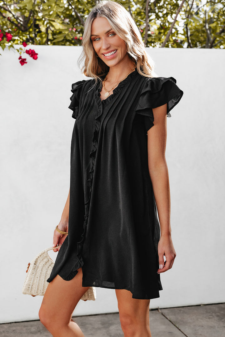 Woman wearing a black dress with ruffled sleeves against a white wall.