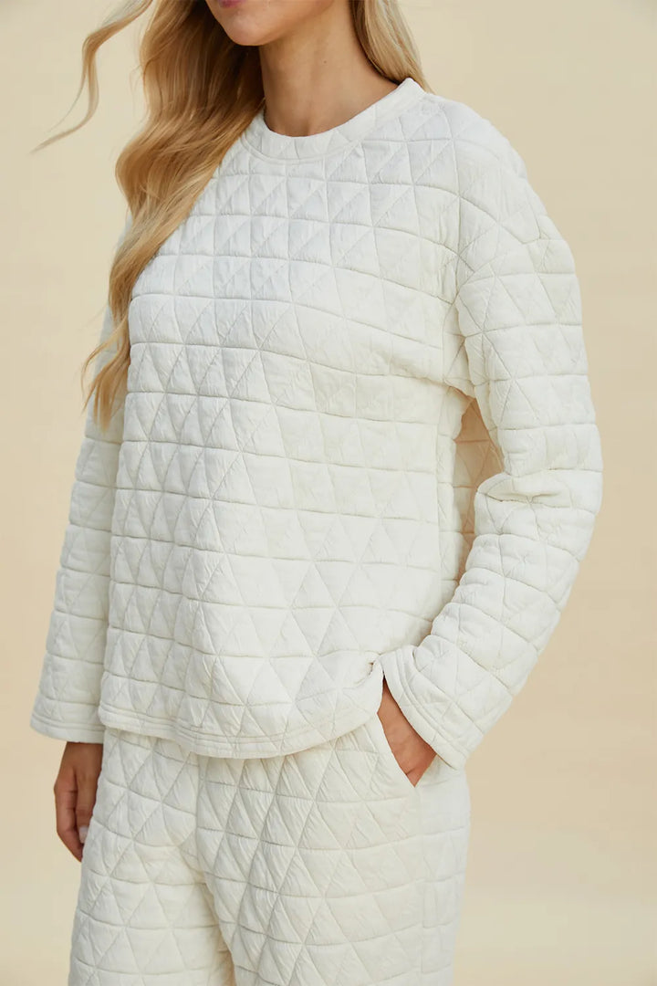 Person wearing a quilted white sweater and pants on a beige background