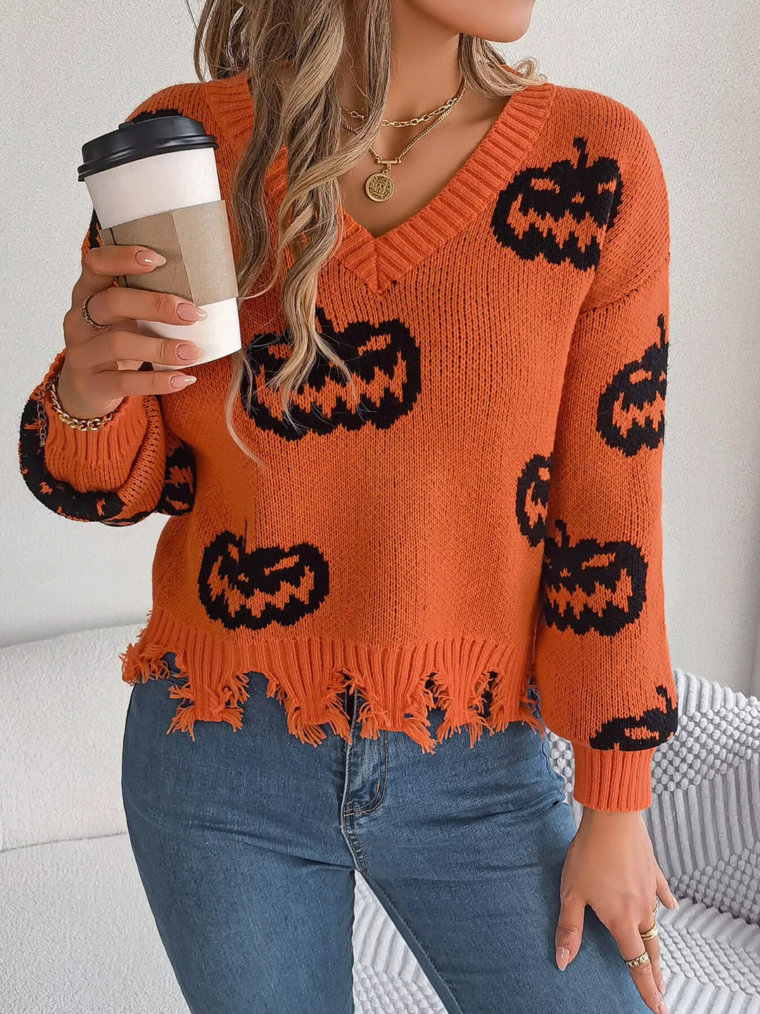 Women wearing orange sweater with black pumpkins on it while holding a cup