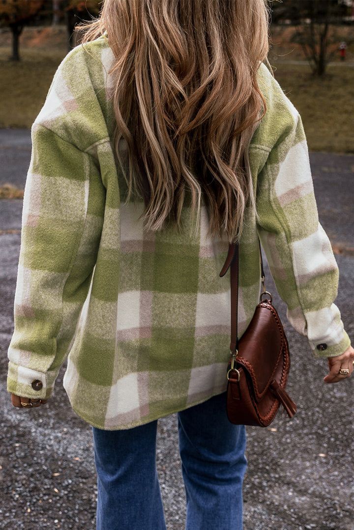 Person wearing a green and white plaid coat with a brown leather bag outdoors.