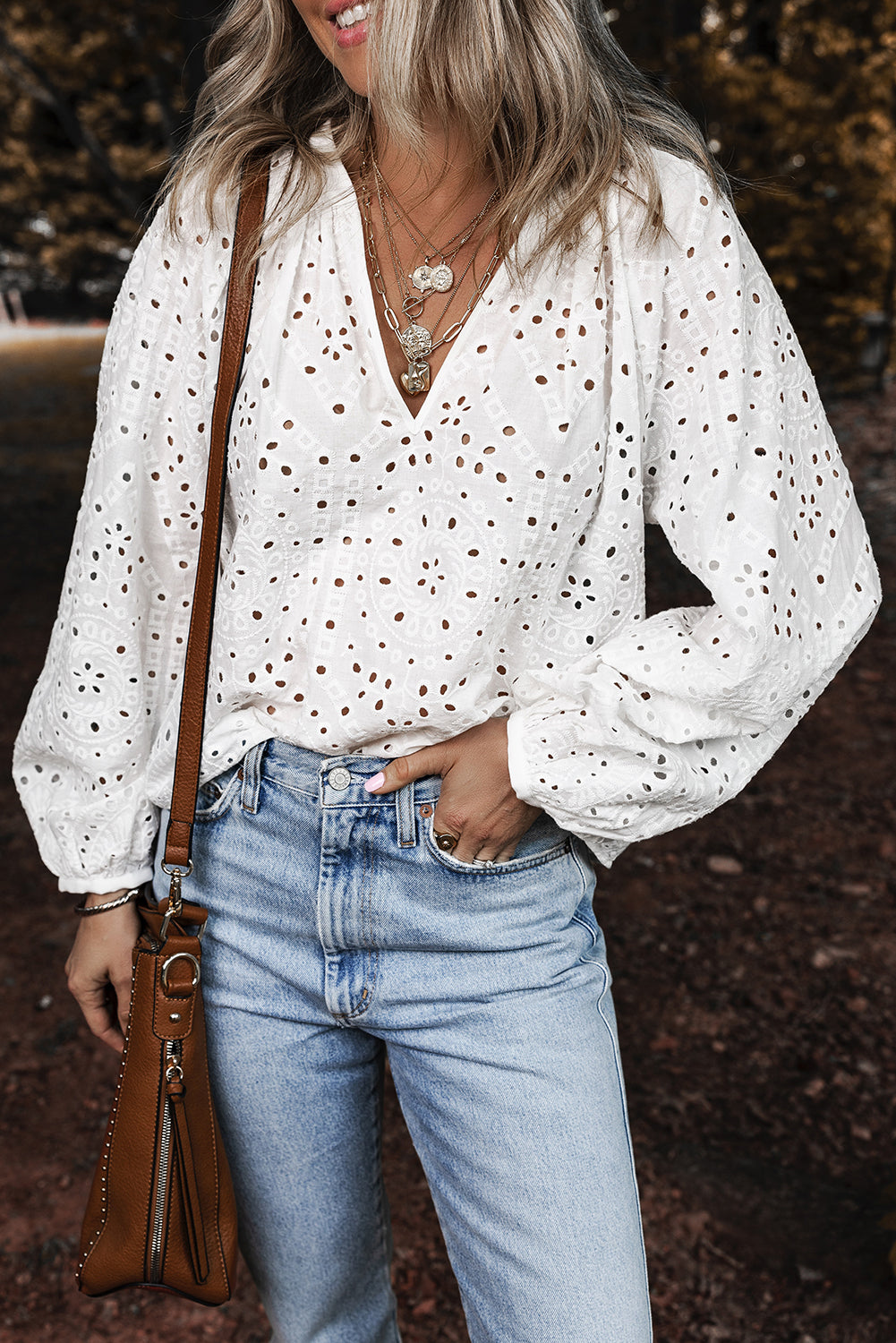 Woman wearing a white blouse and blue jeans, holding a brown leather bag.