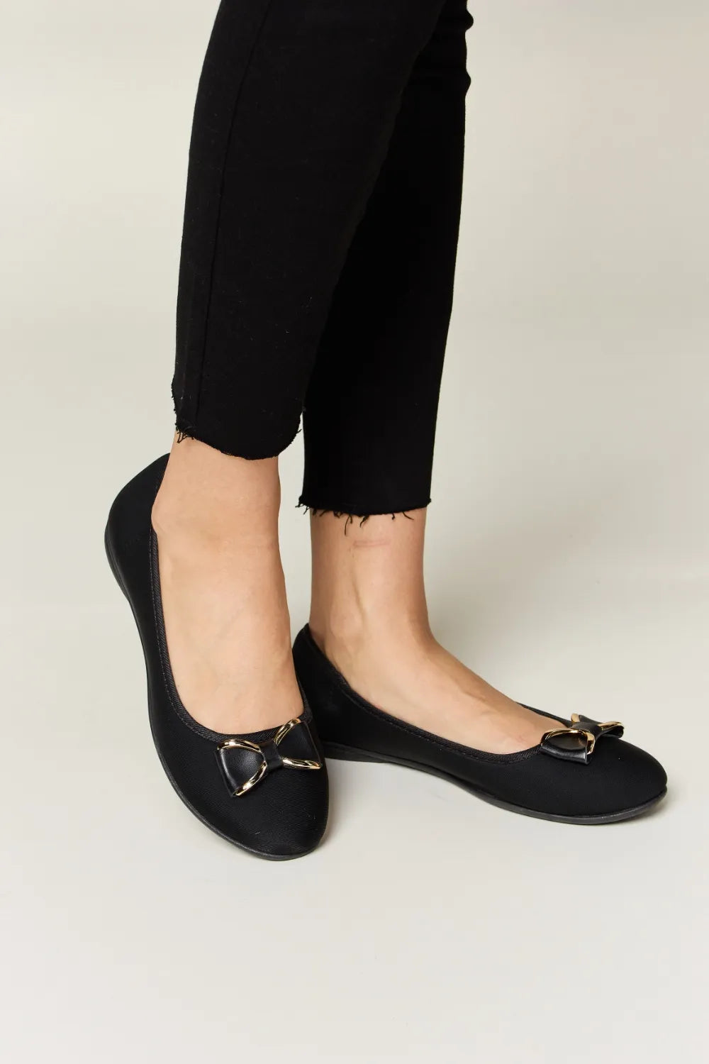 Black flat shoes with decorative buckles worn with black pants on a light background