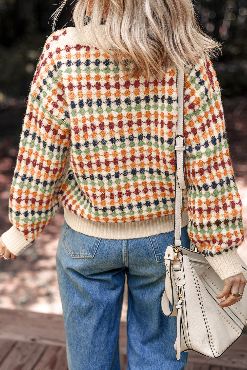 Person wearing a colorful patterned sweater and blue jeans, holding a beige handbag.