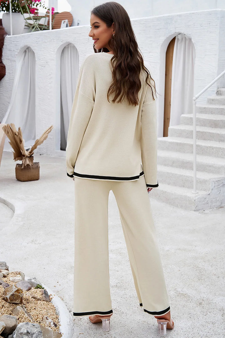 Woman in a cream outfit with black trim standing on a white staircase.