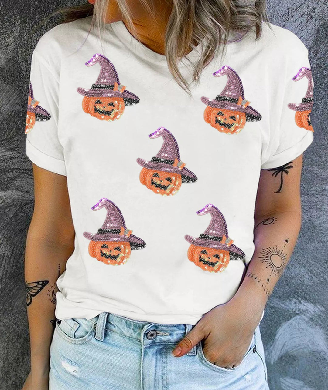 Women wearing white tee shirt with sequence pumpkins wearing a purple sequence hat while right hand is tucked in jean pocket