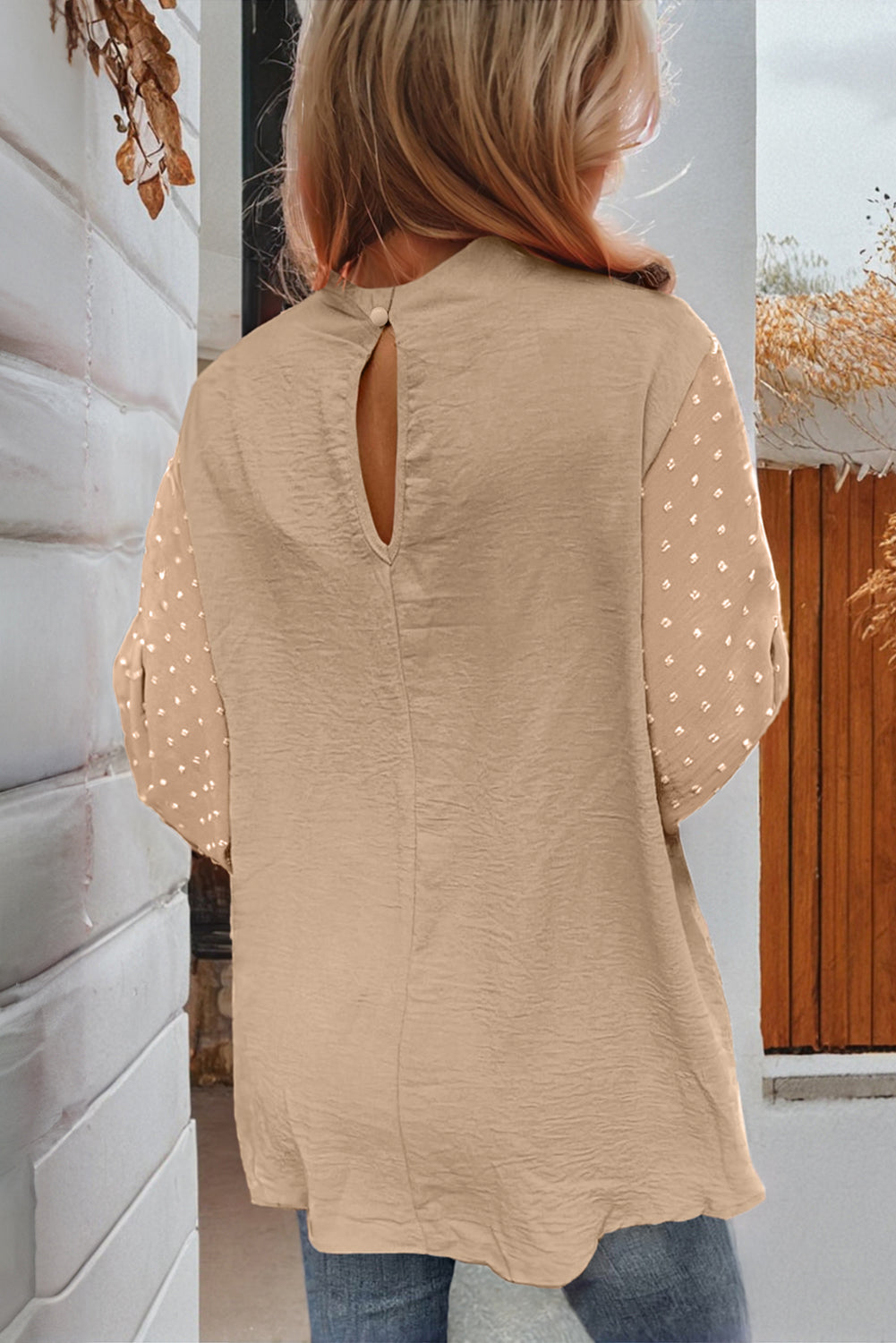 Person wearing a beige blouse with a cut-out back design, standing in a neutral indoor setting.