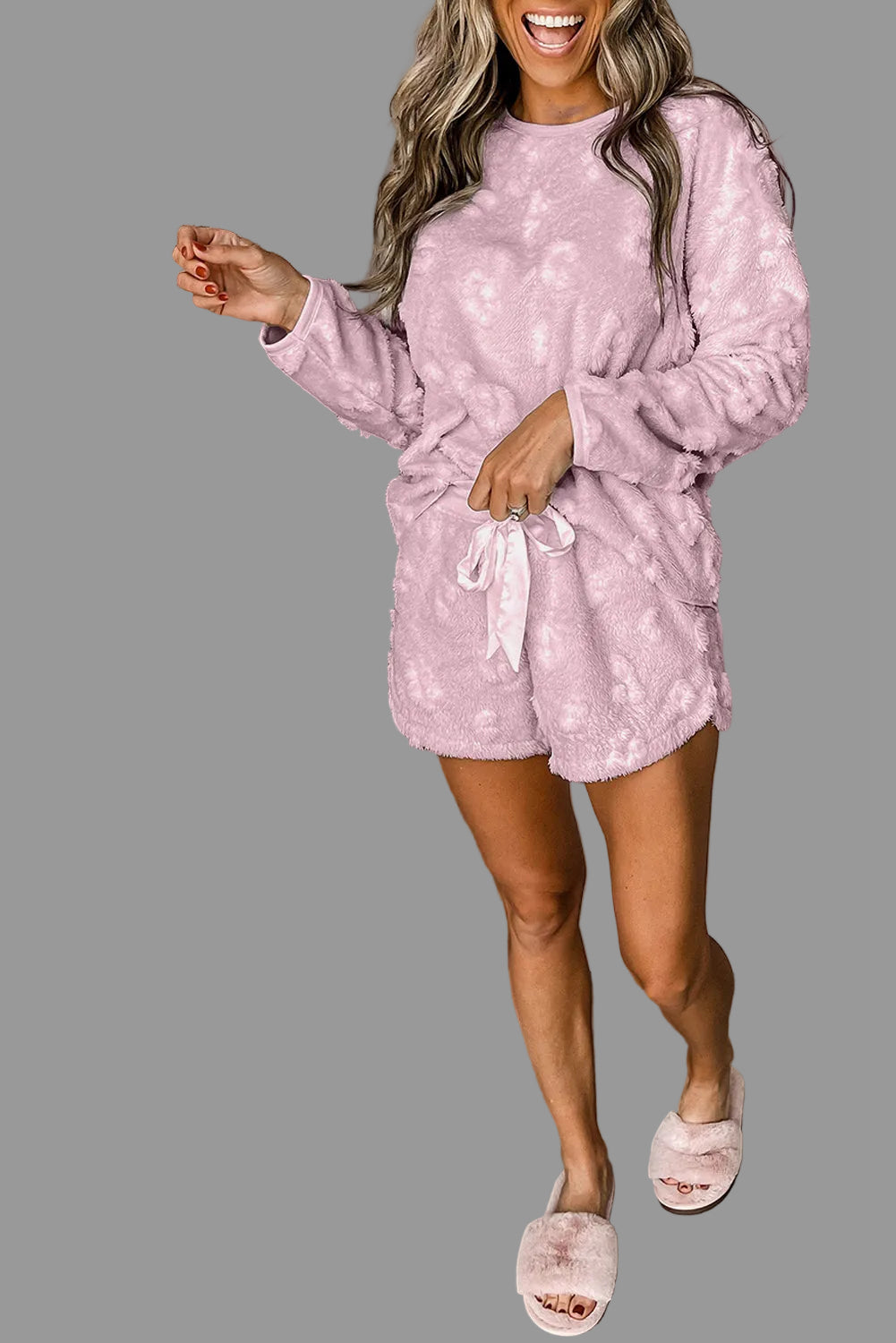 Woman in pink pajama set standing next to a gray wall.