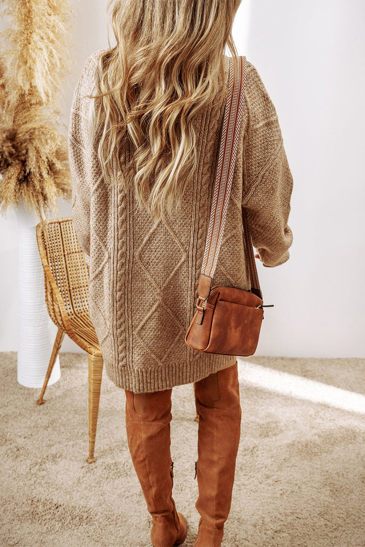 Person wearing a beige cardigan dress and brown boots, holding a brown handbag indoors.