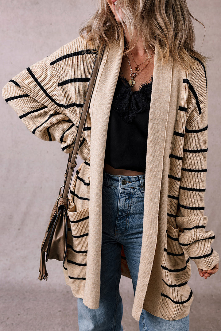 Person wearing a beige cardigan with black stripes, holding a brown handbag against a neutral background