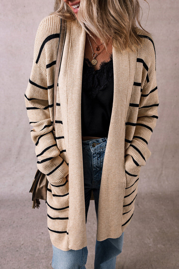 Person wearing a beige cardigan with black stripes, black top, and blue jeans against a neutral background