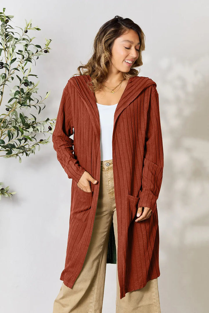 Woman wearing a long rust-colored cardigan against a light background