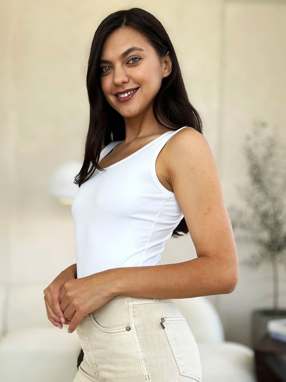 Woman wearing a white sleeveless top and light-colored pants against a neutral background