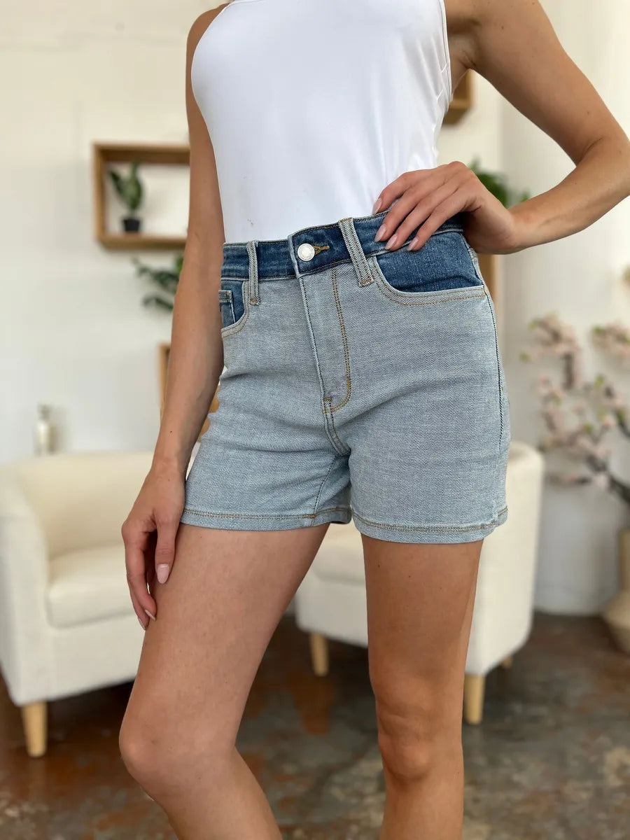 Person wearing light blue denim shorts and a white top in a blurred indoor setting