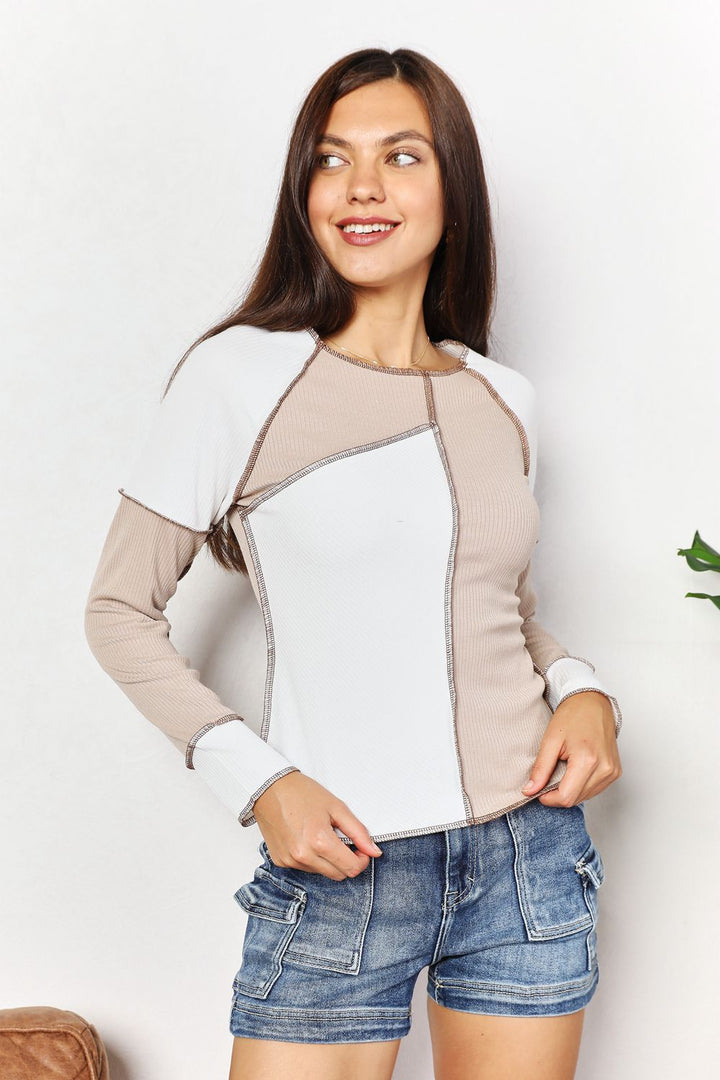 Woman wearing a two-tone top with beige and white panels on a plain background