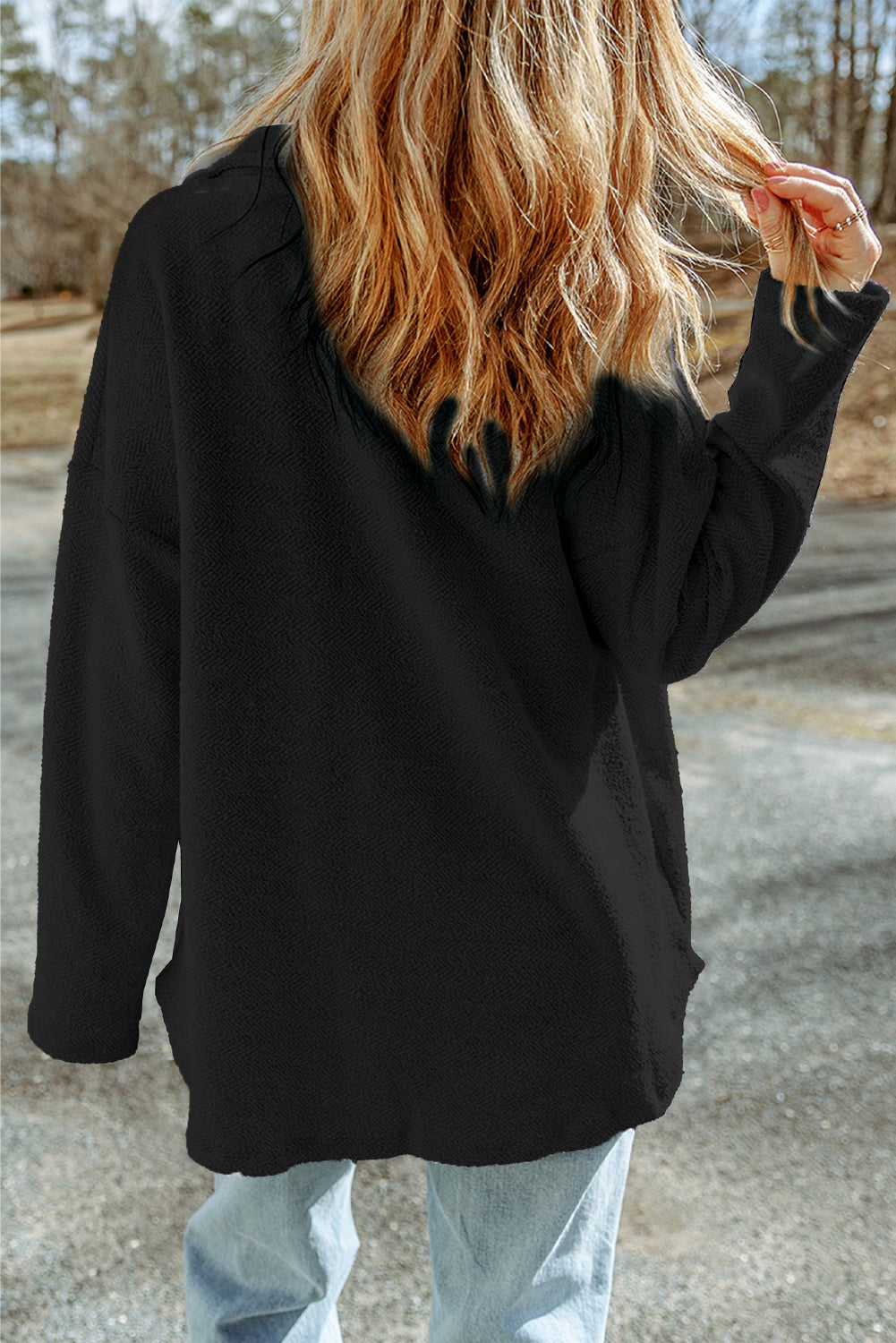 Person wearing a black hoodie outdoors on a road with trees in the background