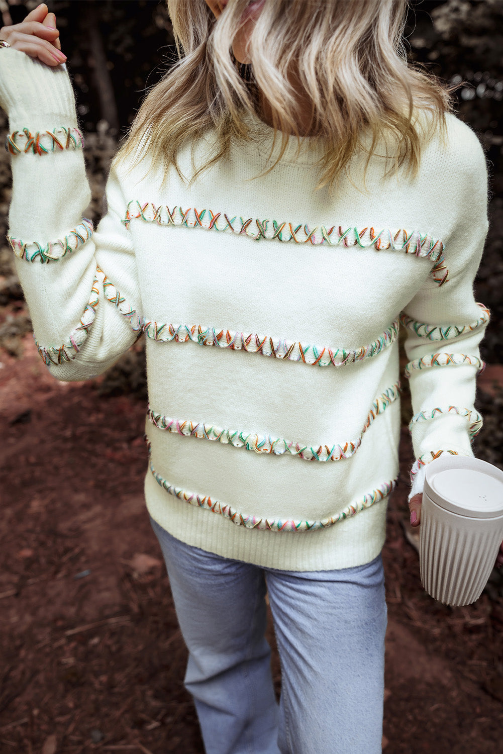 Person wearing a white sweater with colorful patterns outdoors.
