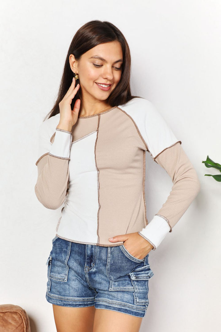 Woman wearing a beige and white long-sleeve top with denim shorts on a light background