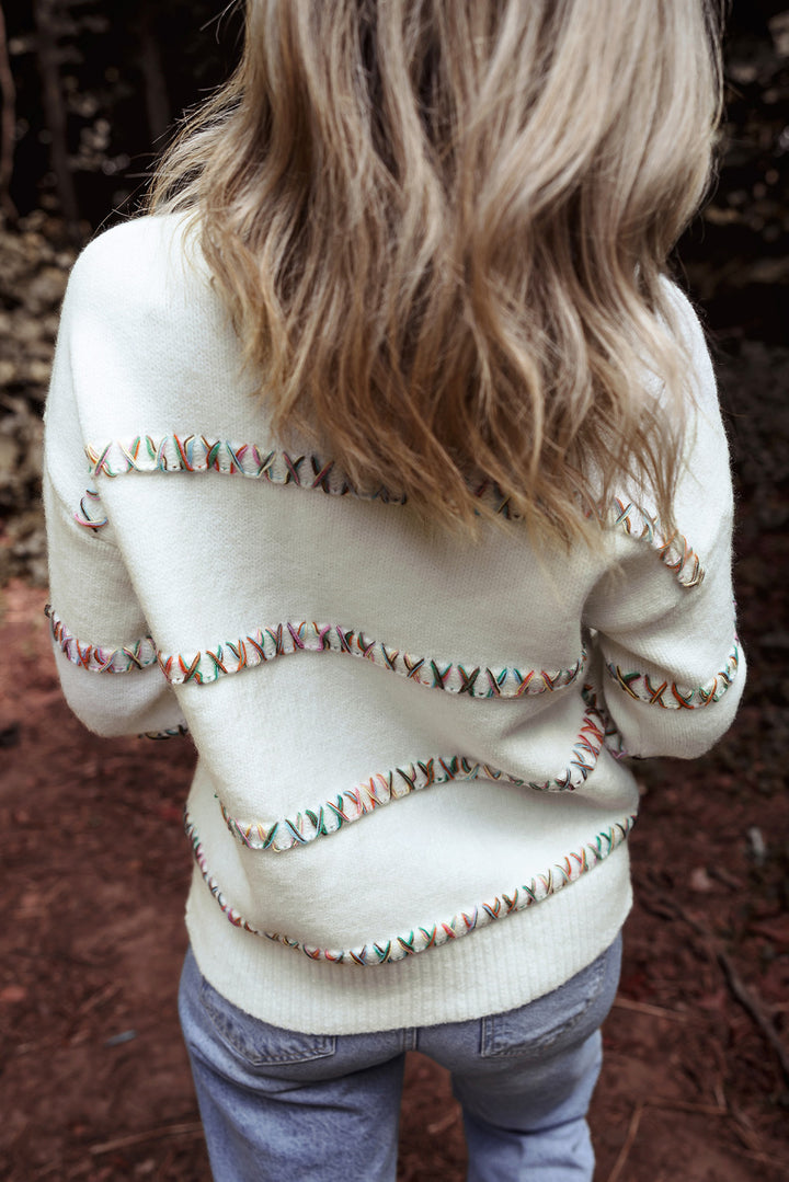 Person wearing a white sweater with decorative buttons in a natural setting