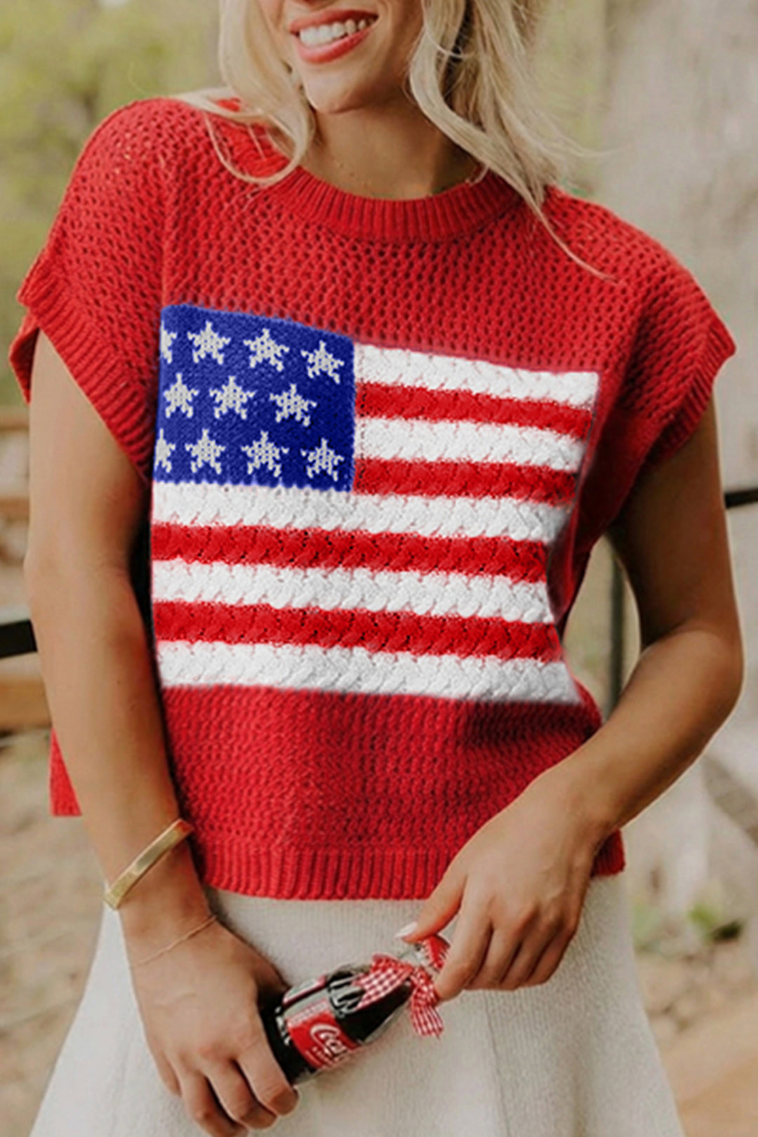 Person wearing a red sweater with an American flag design, holding a Coca-Cola bottle.