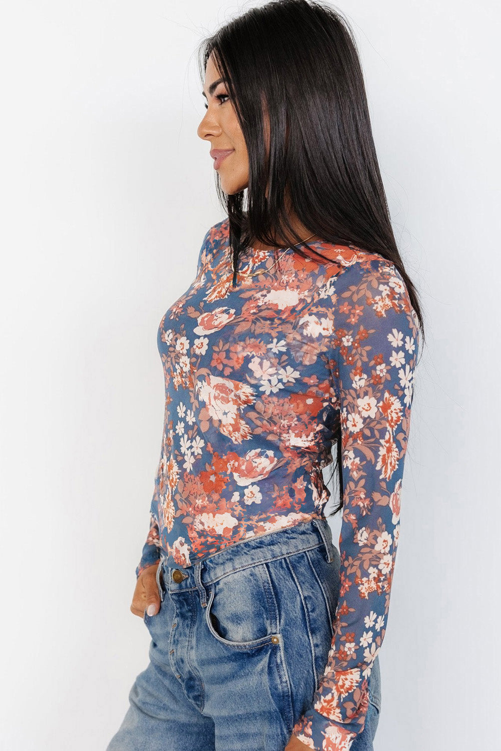 Woman wearing a floral long-sleeve top and jeans against a white background
