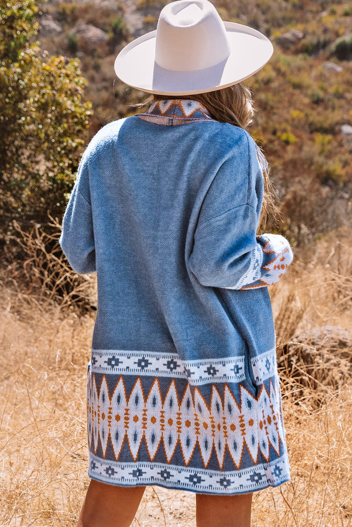 Person wearing a blue patterned cardigan and beige hat in a natural setting