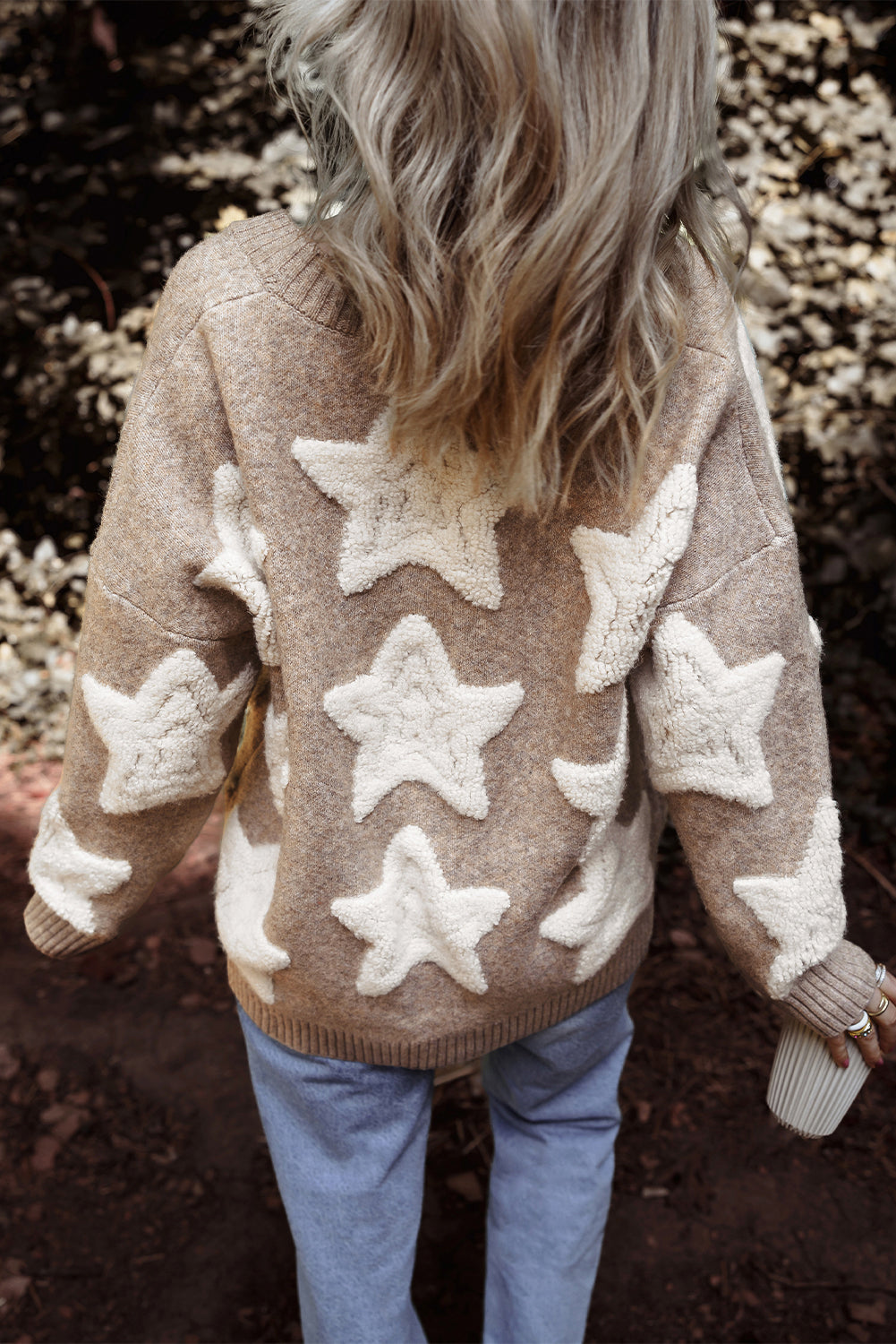 Person wearing a beige sweater with star patterns in an outdoor setting