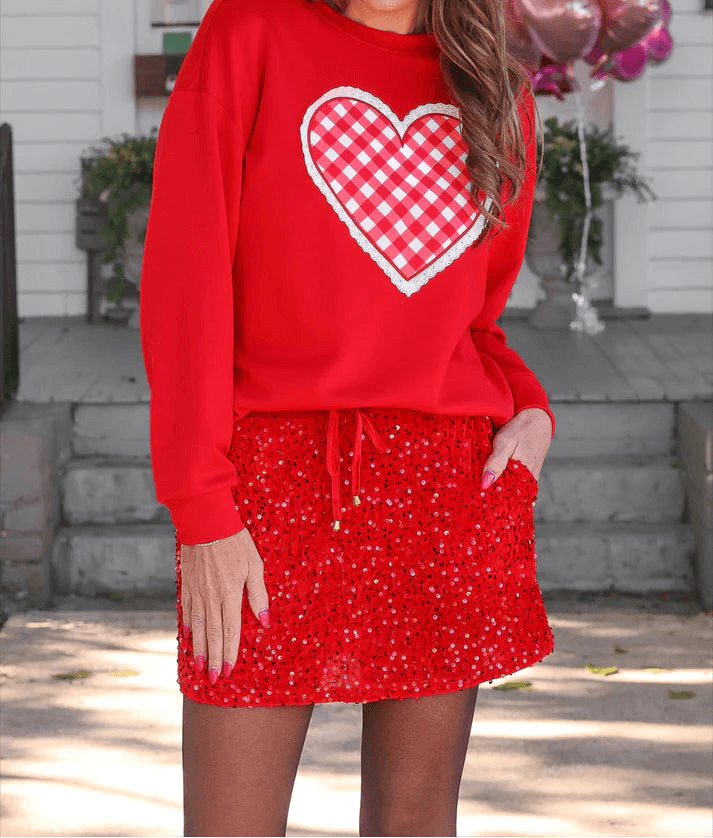 Woman wearing a red sweatshirt with a heart design and a matching skirt outdoors.