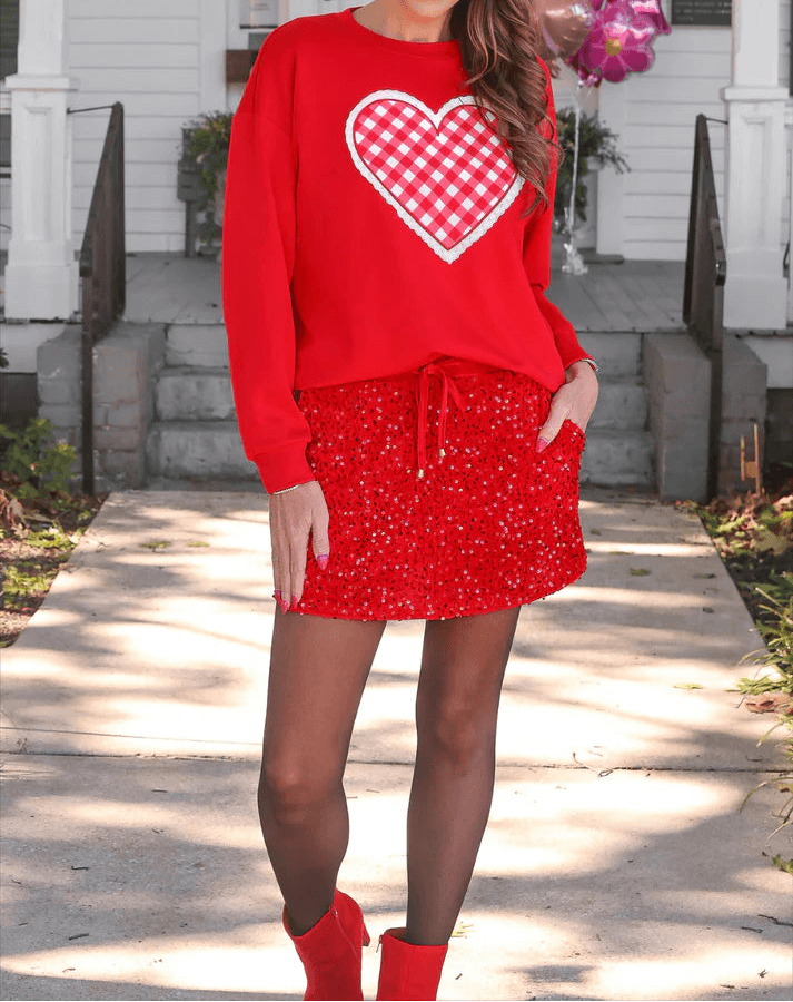 Woman wearing a red outfit with a heart design in front of a house.