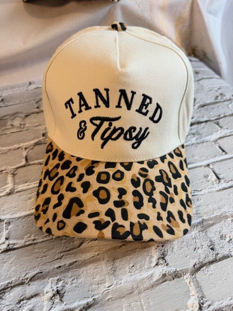 Beige cap with leopard print brim and 'Tanned & Tipsy' text on a stone surface