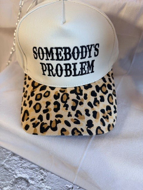 Cap with leopard print visor and 'SOMEBODY'S PROBLEM' text on a white background