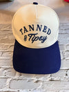 Cap with 'Tanned & Tipsy' text on a textured wall background