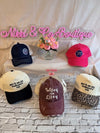 Collection of baseball caps with text on a table with flowers and 'Nikel & Co Boutique' sign.