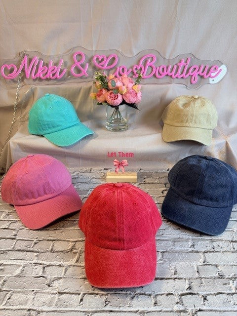 Colorful baseball caps on a table with 'Nikki & Lee Boutique' sign in the background.